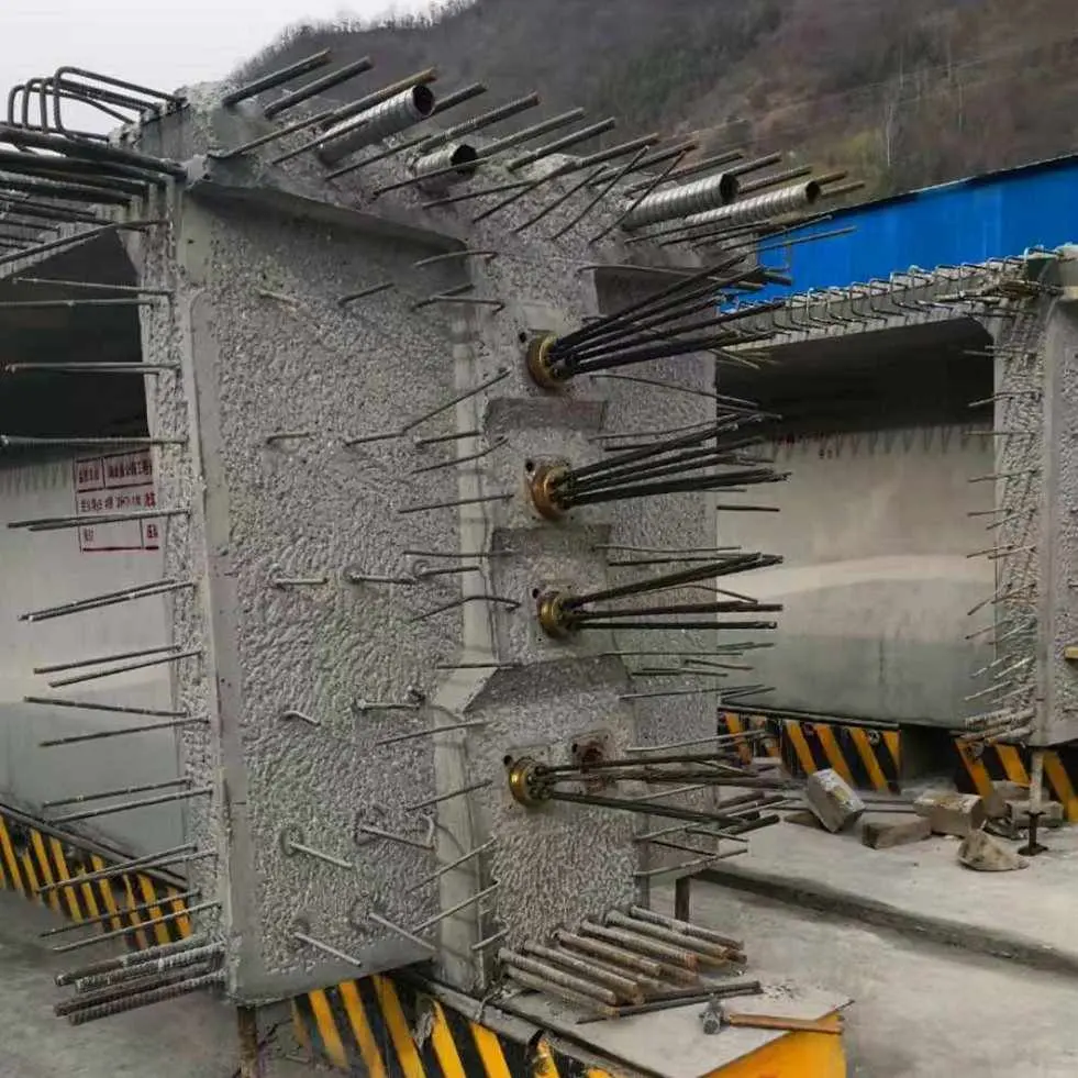 Beton köprü kirişinin ankraj yüzü: beton yüzeyinden çıkan çok sayıda PT tendon ankraj ucu, sarı gerdirme krikolarına bağlanmış; arkada köprü kemeri ve dağlar