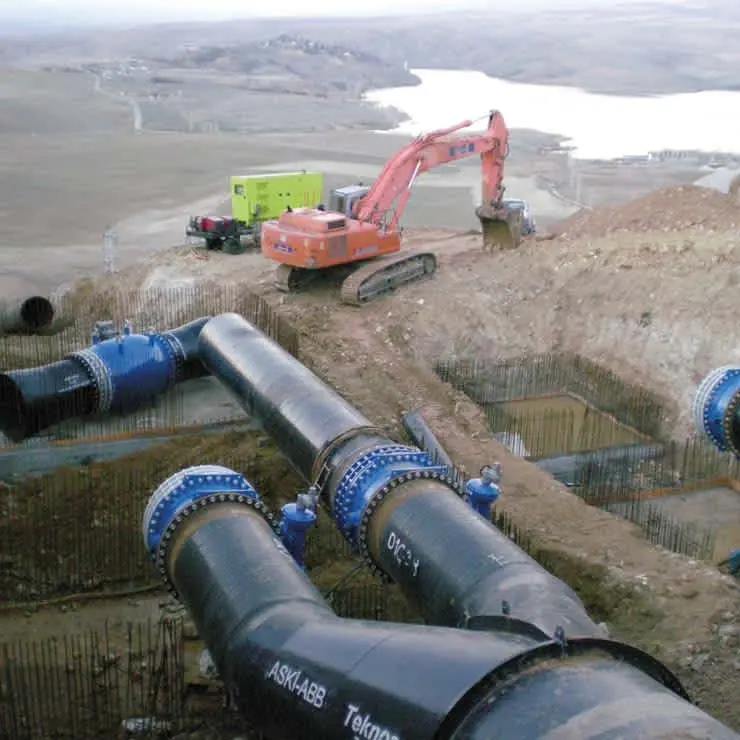 ASKI-ABB büyük çaplı çelik iletim boruları inşaat sahası — mavi flanşlı boru hattı, ekskavatör ve arka planda gölet
