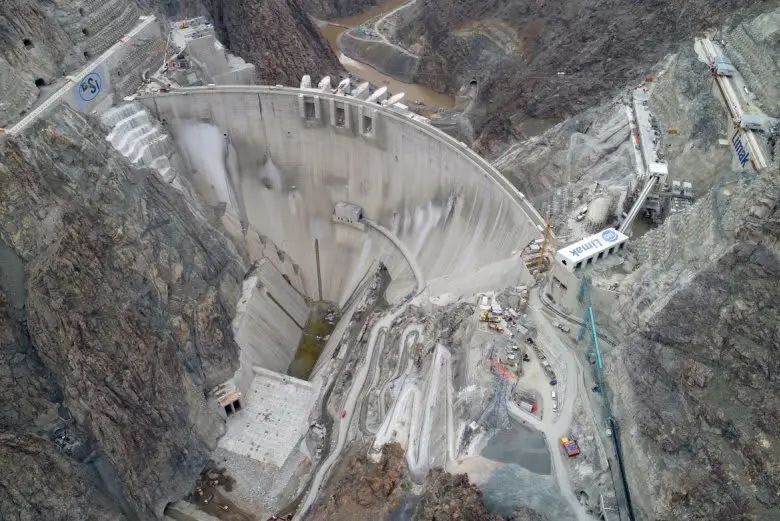 İnşaat halindeki büyük kemer beton baraj havadan fotoğrafı — derin kaya vadisi, kemer geometrisi ve yan tünel girişleri