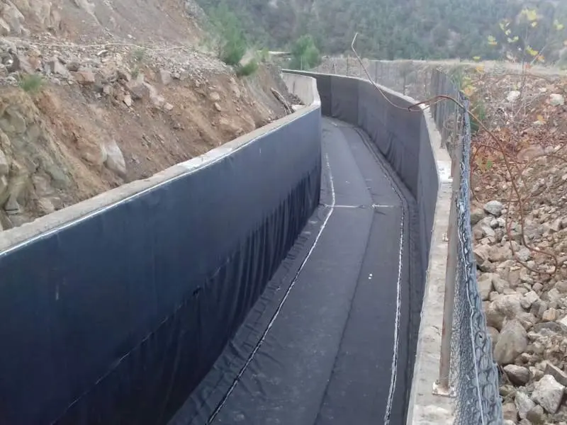 Kayalık vadi içinde betonarme kanal üzerine siyah HDPE jeomembran kaplama saha fotoğrafı — eğimli yamaç ve taban kaplama