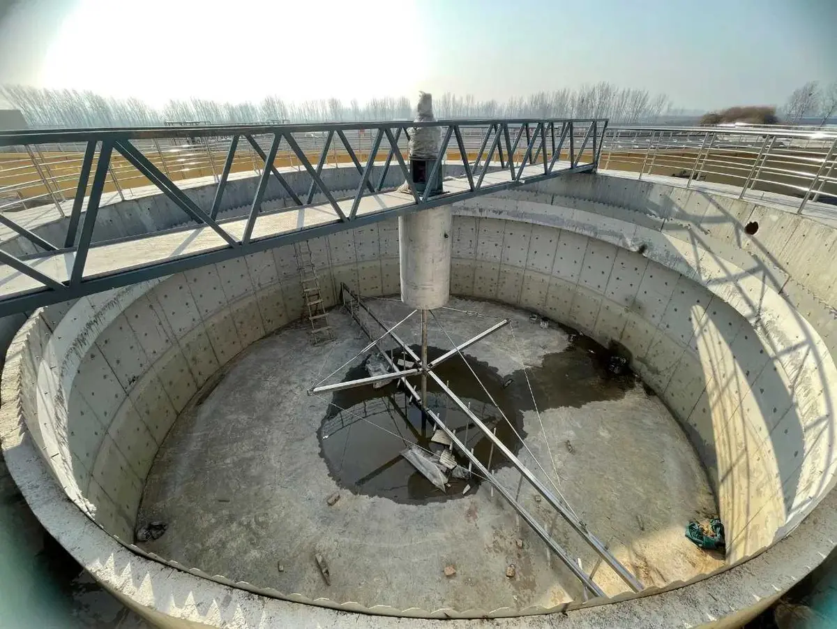 İnşaat halinde dairesel çöktürme havuzu — çelik çamur toplama köprüsü, merkezi sürücü ve döner kazıyıcı kolu, beton tank