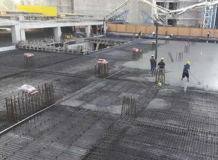 Büyük ölçekli birleşik temel ve döşeme inşaatında beton dökümü: geniş donatılı zemin üzerinde beton pompasıyla döküm, işçiler vibratörle sıkıştırma yapıyor