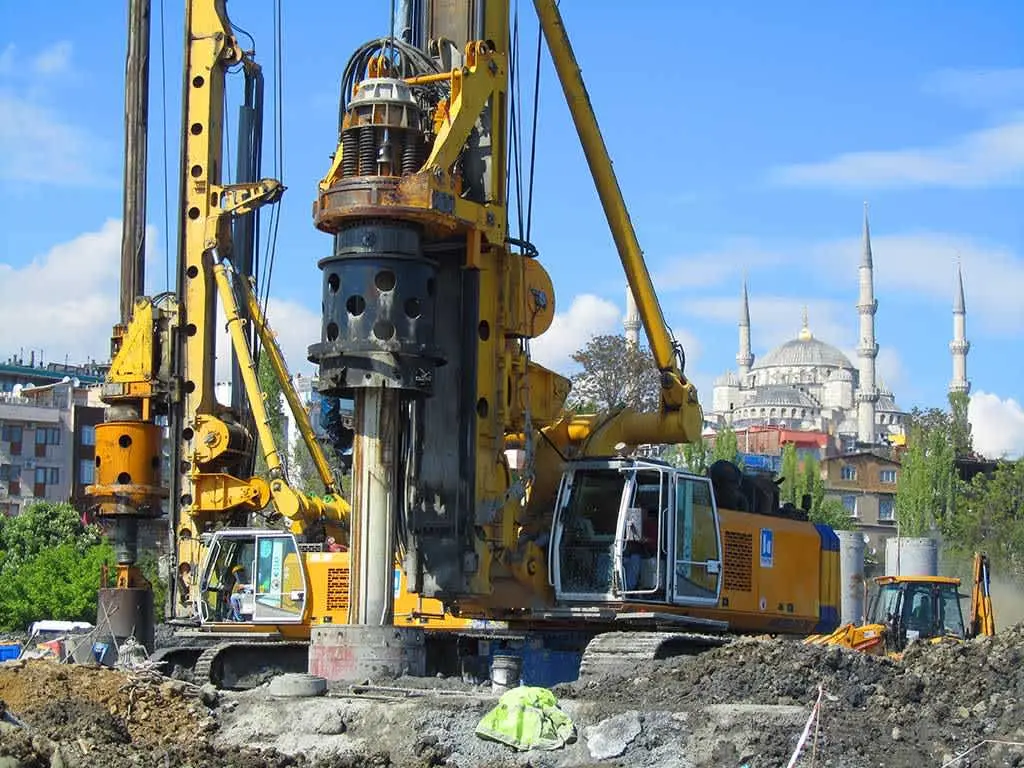 İstanbul'da tarihi Sultanahmet Camii arka planında fore kazık delme makinesi çalışıyor; sarı-turuncu renkte büyük döner başlıklı delme kulesi ve sondaj aparatı, yanında inşaat ekipmanları ve insan silüetleri