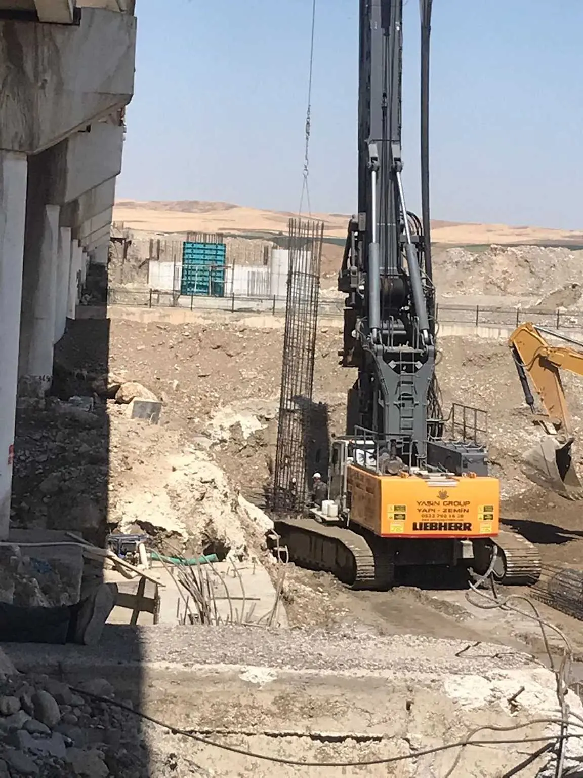 Türkiye'de kuru iklimde fore kazık delgi makinesi, bina bodrum kazısı kenarında çalışıyor; Liebherr markalı siyah renkli kazık makinesi, yanında kazık donatı kafesleri ve kazı alanı görülmektedir