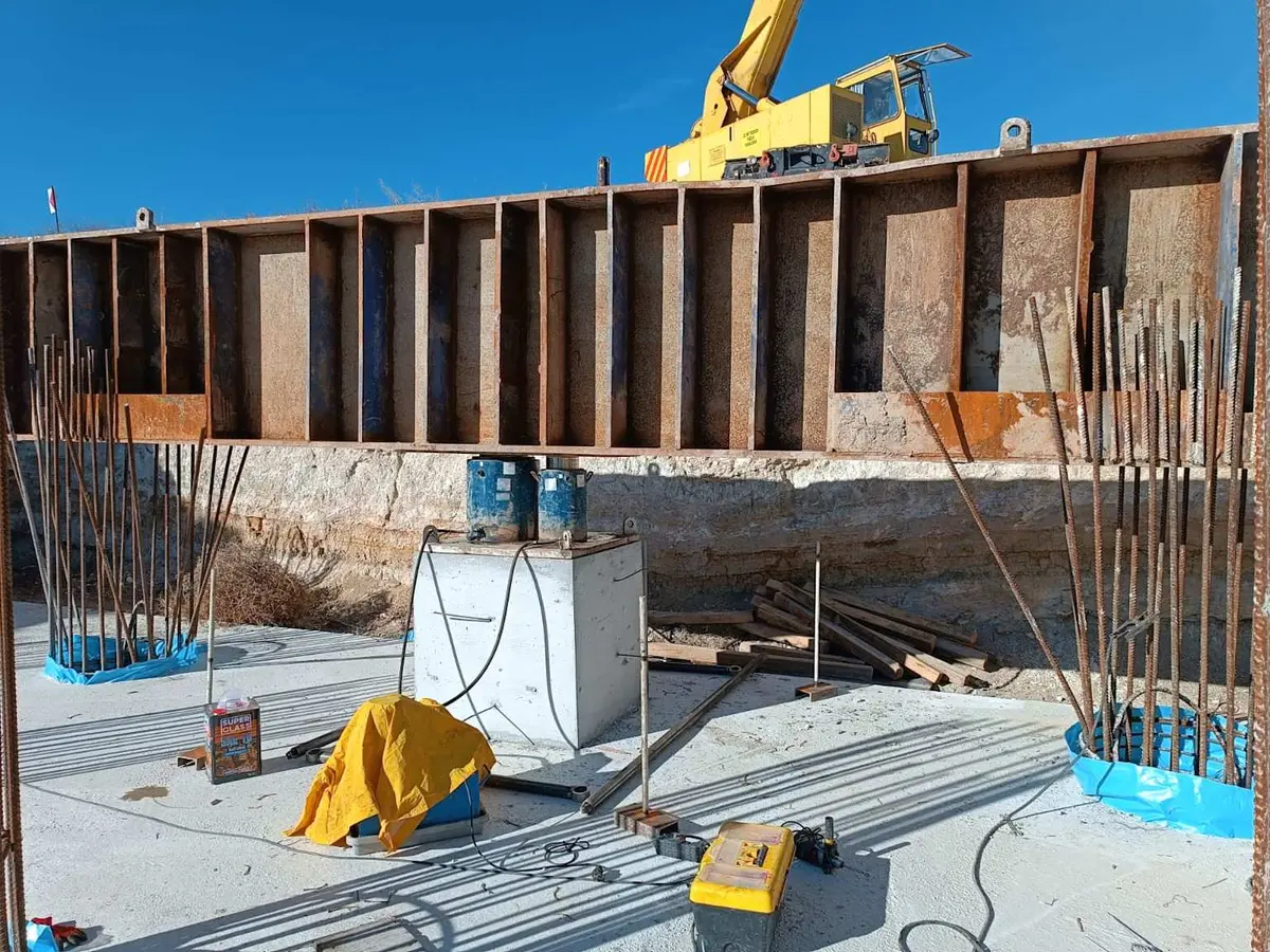 Betonarme istinat duvarı ve fore kazık inşaatı: sarı vinç, ahşap kalıp panelleri, zemine çakılmış donatılı kazıklar