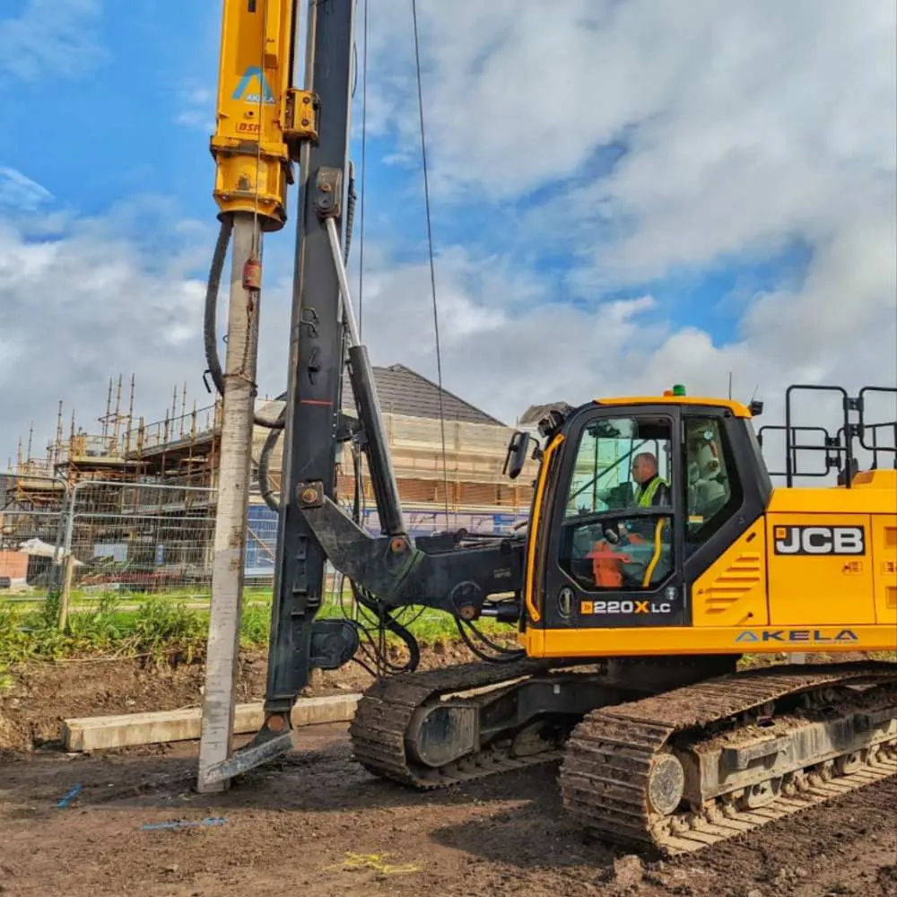 JCB B220XLC kazık delgi makinesi şantiyede çakma kazık imalatı — turuncu JCB ekipmanı, arka planda yapı iskeleti