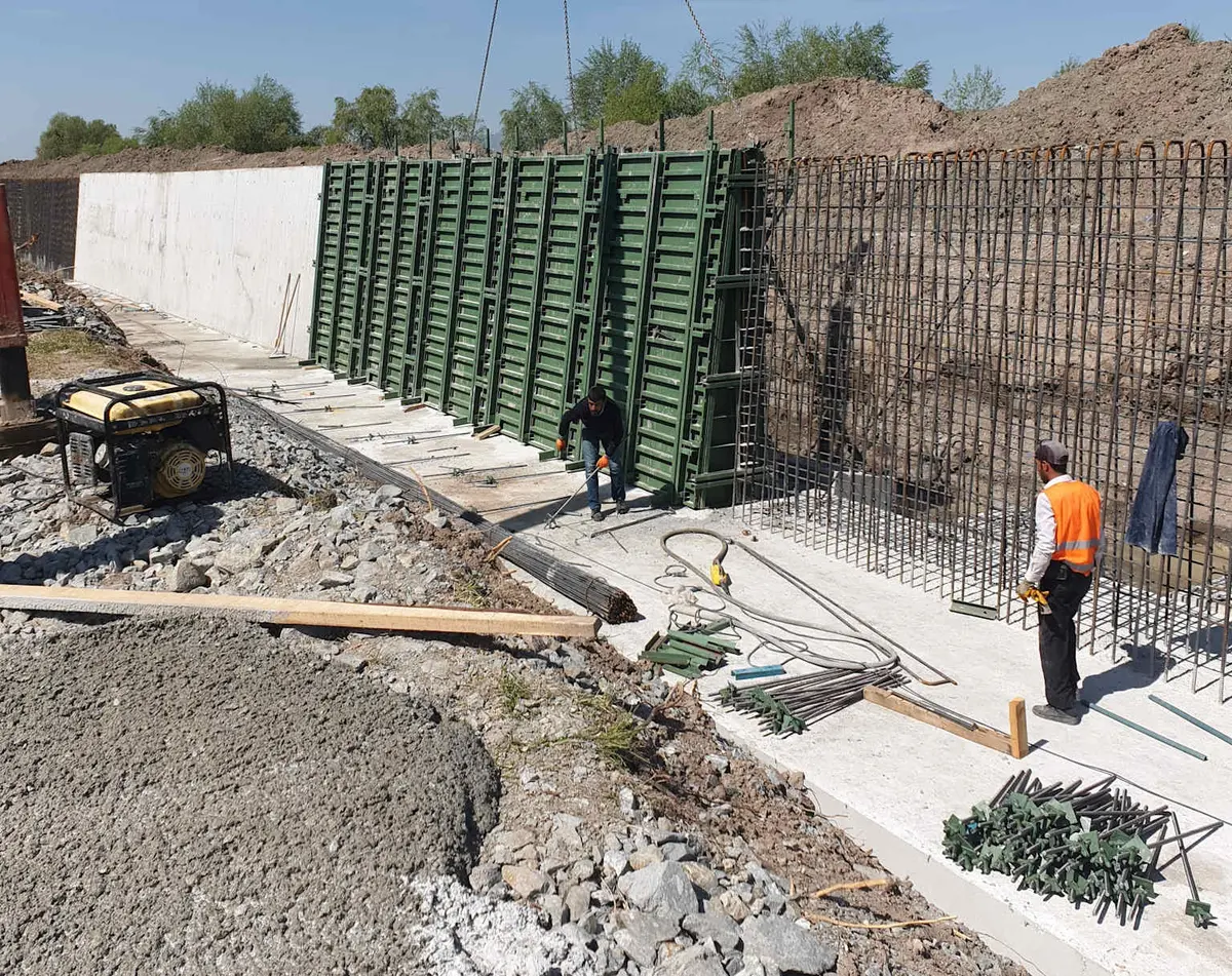 Betonarme istinat duvarı inşaatı şantiyesinde yeşil metal kalıp sistemi ve donatı kafesleri