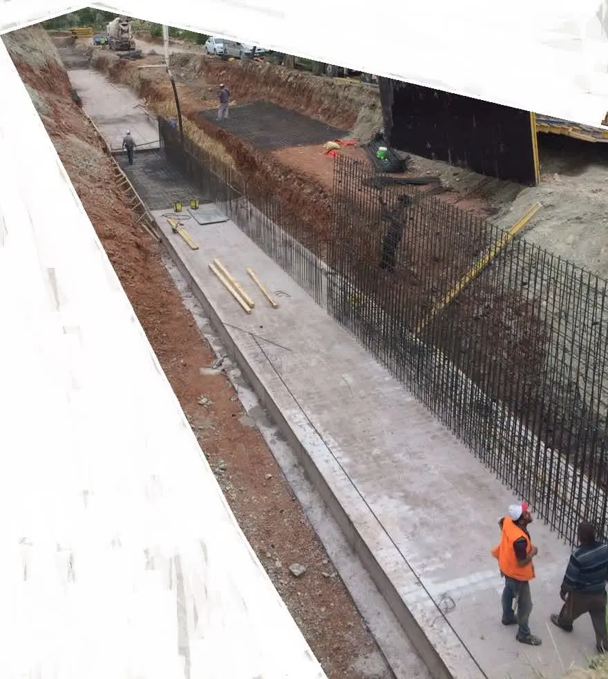 Türkiye şantiyesinde uzun BA konsol istinat duvarı inşaat alanı havadan görünüş: taban beton dökülmüş, donatı kafesleri hazırlanıyor, kırmızı toprak kazı alanı ve iş makineleri görülüyor
