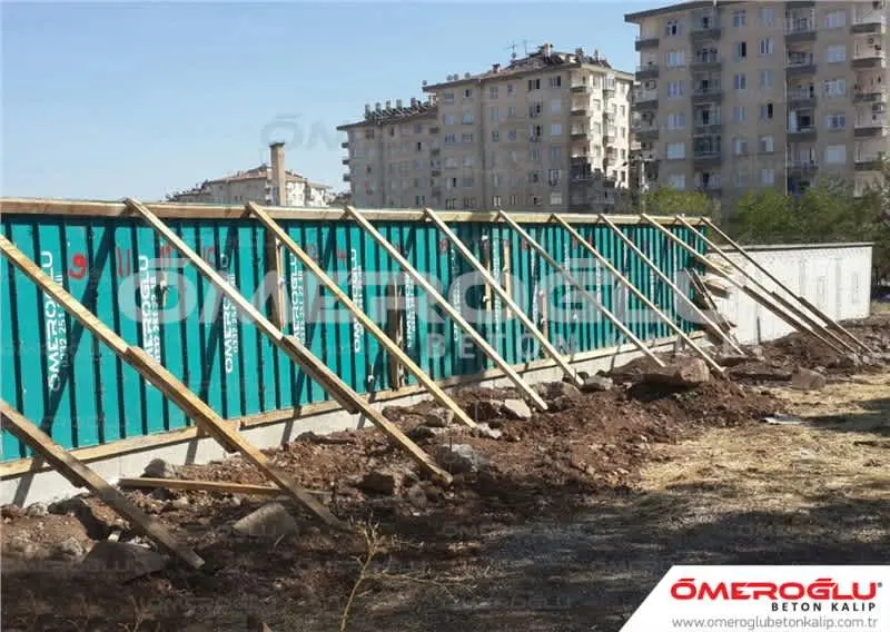 İstinat duvarı kalıp inşaatı — turkuaz beton kalıp panelleri, ahşap destekler, arka dolgu granüler malzeme