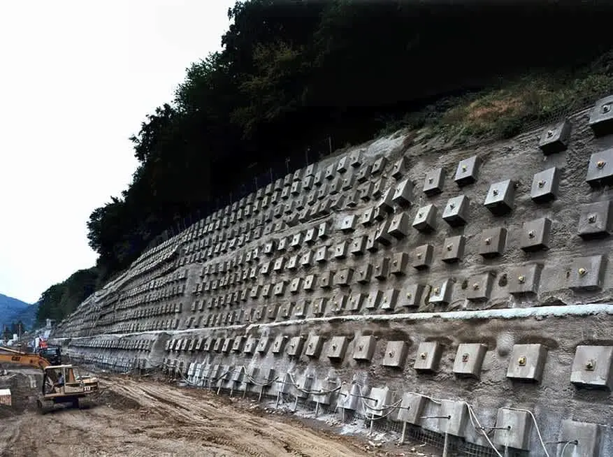 Büyük zemin çivisi duvarı — çivi başlık plakalarının ızgara şeklinde dizildiği geniş beton shotcrete yüzey, tamamlanmış kalıcı zemin çivisi sistemi