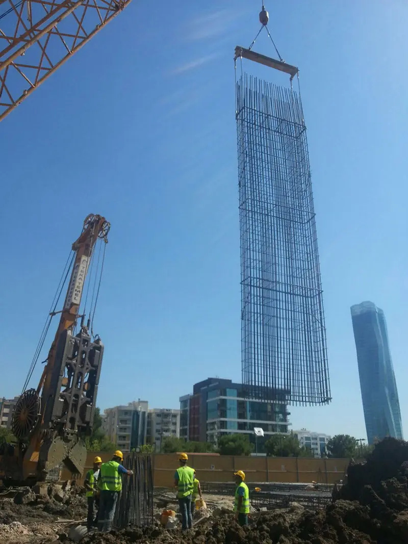 Büyük betonarme donatı kafesi vinçle kaldırılıyor — dikey ve yatay donatı çubukları panel kazısına indirilmek üzere