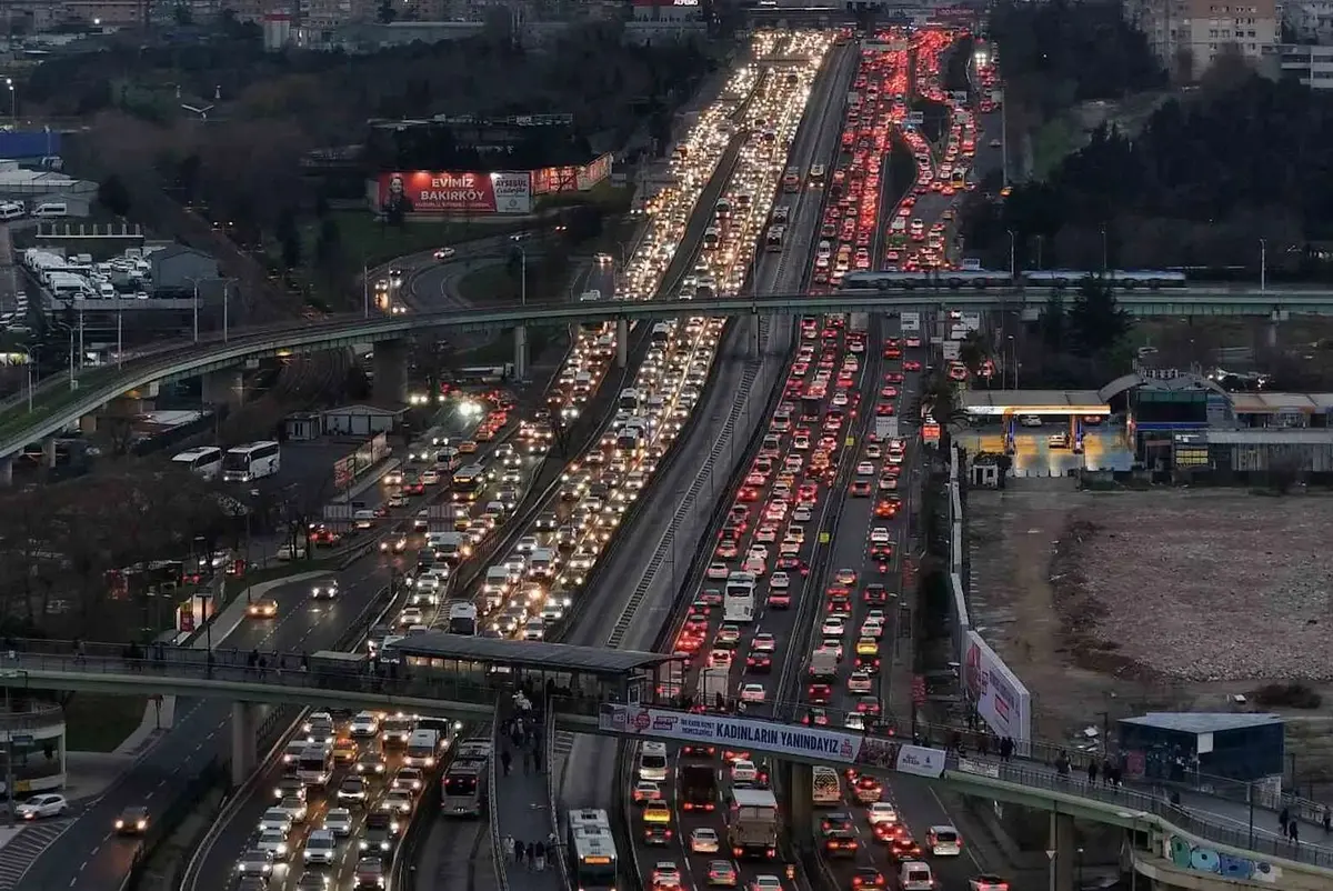 İstanbul'da akşam zirve saatinde çok şeritli köprü ve otoyol geçişinde yoğun trafik: her iki yönde de kalabalık trafik kolonu, kırmızı stop ışıkları, alacakaranlık arka planı, köprü çelik kirişleri görünmektedir; LOS E-F koşullarını temsil eden kentsel trafik doygunluğu