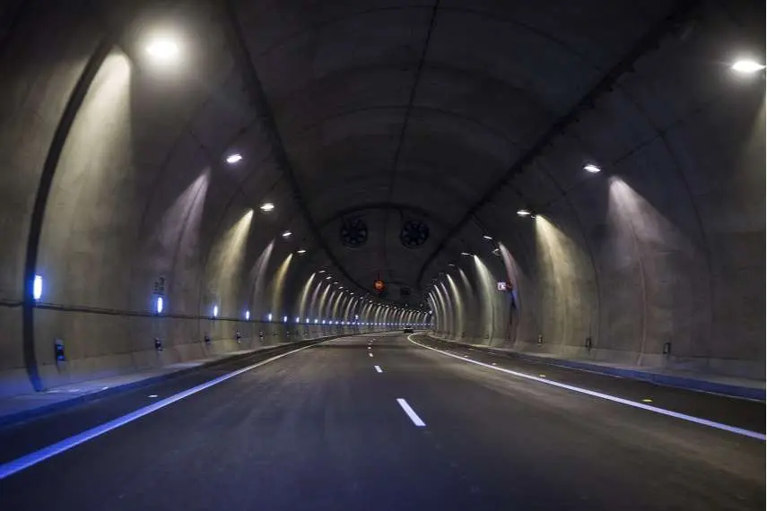 İki şeritli karayolu tüneli içeriden görünüm; tavan kemerinde dairesel jet fanlar, yan duvarlarda LED şerit aydınlatma, beton duvar yüzeyi ve uzayan tünel perspektifi