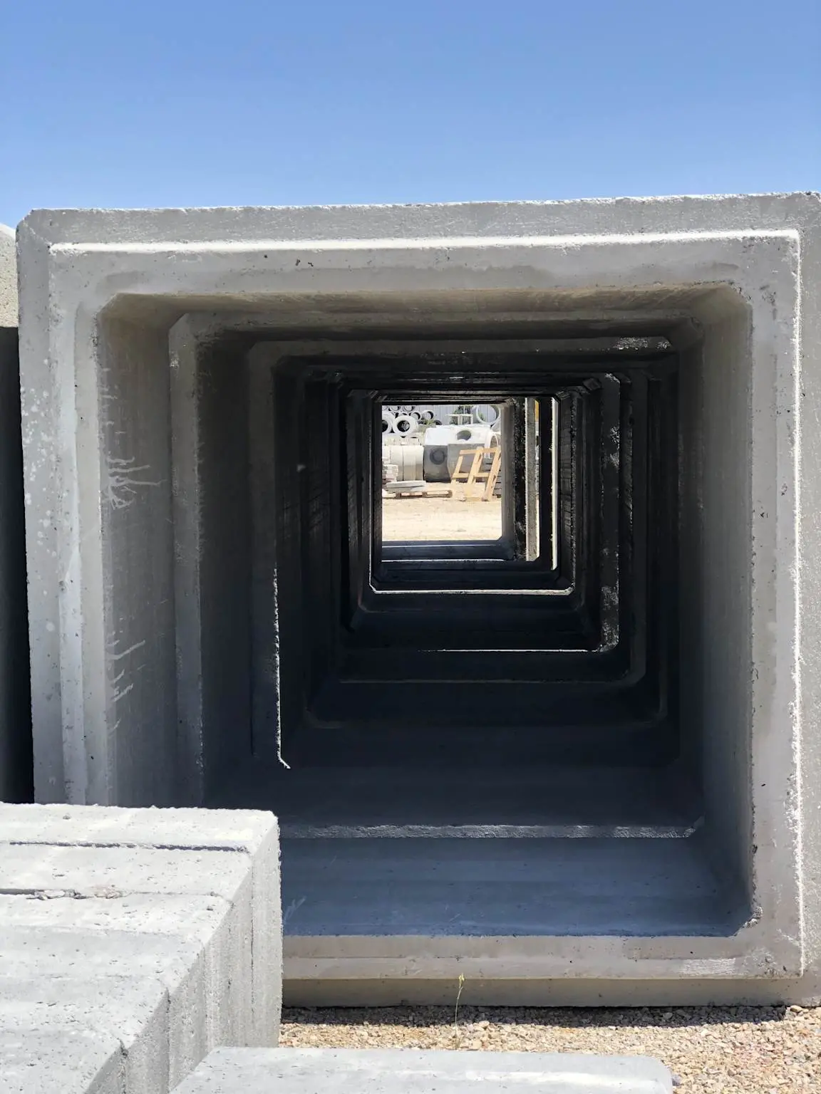 Açık hava depolama alanında yan yana dizilmiş prefabrik betonarme kutu menfez elemanları; içeriden bakış açısıyla iç içe geçmiş kare kesit zincirleme görünümü