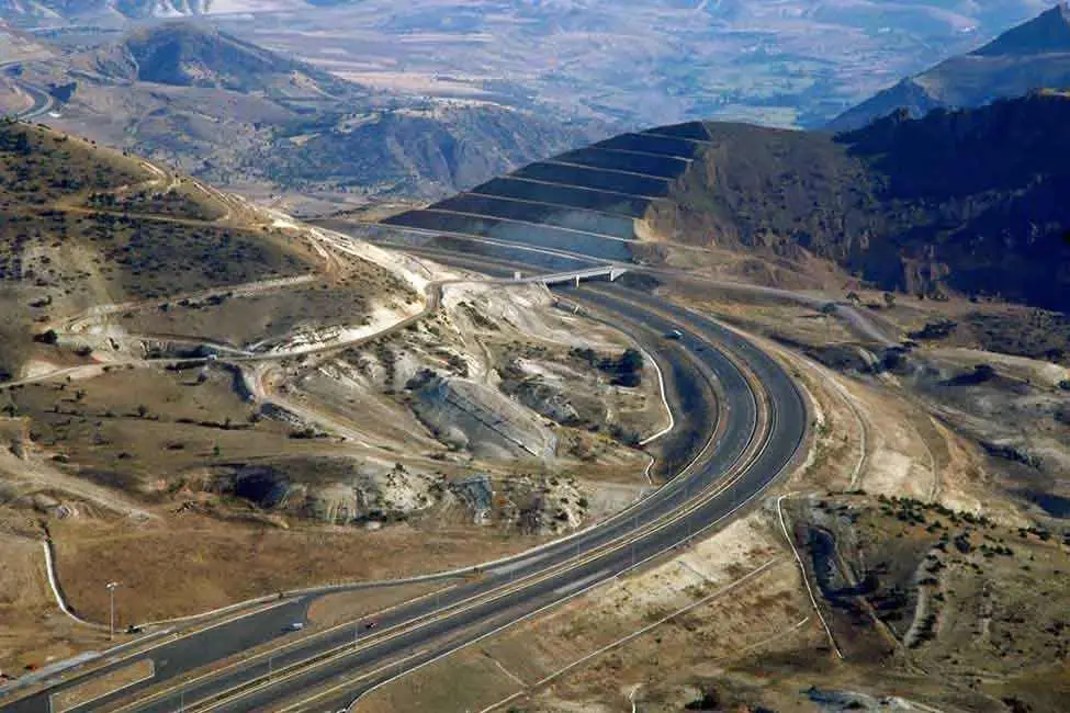Türkiye dağlık arazisinde devlet yolu: sarp vadi içinde kıvrımlı yol güzergahı, viyadük köprü ve şev kesmeleri — KGM dağlık arazi standartları uygulanan proje